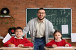 © Pixel-Shot - Happy music teacher with young students in classroom learning musical notes and theory, a chalkboard with musical staff and notes is visible in the background, indicating a focus on music education