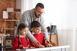 © Pixel-Shot - Music education and childhood development: teacher guiding young students learning piano keys in a home setting, a male instructor helps a boy and a girl practice playing a musical keyboard
