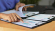 © Siwaporn - Healthcare professional reviewing analytical reports and performance charts on documents, supporting medical administration, healthcare data analysis, strategic planning, and operational decision