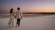 © Nathaniel - A young couple holding hands walking across a vast sandy desert at sunset