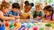 © ISVO - Multicultural children painting a colorful rainbow with handprints on a large sheet of paper at a bright classroom table surrounded by art supplies and plants