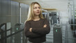 © Krakenimages.com - Woman with arms crossed by turnstile in airport terminal, standing alone near security checkpoint and scanners, looking sideways with stern expression; impatience resolve.