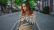 © Krakenimages.com - Woman redhead in striped top points finger down at empty urban street with slight smirk, casual studded belt and jeans visible; skepticism curiosity.