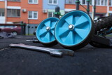 Children bicycle maintenance layout with spanner wrenches and blue training wheels on ground. Close up of kids bike repair tools and multi-tool selector on dark rubber coating background outdoors