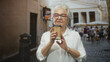 © Krakenimages.com - Elderly woman holding a paper coffee cup, red nails visible on hands, standing in a cobbled street; serenity nostalgia.