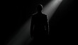 © UD - Businessman stands in a dark room illuminated by a single vertical beam of light that highlights his silhouette against the surrounding shadows while emphasizing his formal attire.