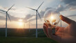 © Lang - Human hand cradling glowing glass lightbulb representing clean renewable energy with solar panels wind turbines and bright sun shining over sustainable green environment landscape background.