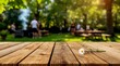 © Alchemy - Single white daisy on a wooden picnic table in a sunny park with blurred people and barbecue smoke in the background