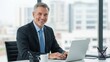 © shinha - Confident senior businessman smiling happily while using a laptop in a bright corporate Wallpaper Background image