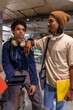 © wavebreak3 - Diverse male students sitting in campus lounge wearing hoodie and headphones, sharing tablet