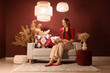 © Pixel-Shot - Smiling woman reading magazine on sofa in cozy living room with bohemian decor and warm lighting