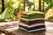 © Watasiwa - Stack of Neatly Folded Outdoor Clothing on Rustic Wood Surrounded by Nature and Camping Gear