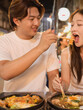 © blueringmedia - Young Asian Man Feeding Street Food to Woman at Night Market