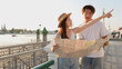 © blueringmedia - Young Couple Consulting Map and Pointing Toward Riverside Temple at Sunset