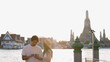 © blueringmedia - Young Asian Couple Using Smartphone by Chao Phraya River with Wat Arun Background
