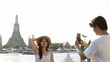© blueringmedia - Young Couple Taking Photos by Wat Arun Temple at Sunset in Bangkok