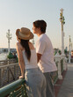 © blueringmedia - Young Asian Couple Leaning on Riverside Railing During Golden Hour