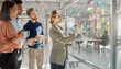 © InfinityVisuals - Team Brainstorming Session: A focused team of professionals collaborates around a glass board, using colorful sticky notes to brainstorm ideas and plan strategies in a modern office setting.