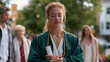 © Tania - University graduate woman standing outside campus gates clutching diploma tube against her chest with eyes shut tight and lips pressed together, family members surrounding her on the sidewalk with e