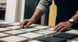 © sukar - A person selecting various square tiles on a table in an interior design setting with hands and watch visible.
