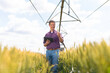 © Dexon Dee - Farmer using tablet in wheat field with irrigation system