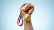 © Saim - Strong hand holding gold medal with ribbon raised high against clear blue background celebrating victory achievement success excellence or professional sports win.
