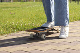 Skater on wooden skateboard, close-up of wheels and deck. Close-up of female legs in white sneakers on skateboard, selective focus. Low angle view of skateboard while skating. Active recreation