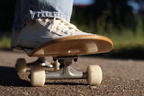 Skater on wooden skateboard, close-up of wheels and deck. Close-up of female legs in white sneakers on skateboard, selective focus. Low angle view of skateboard while skating. Active recreation