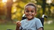 © Dream Studio - Portrait of a happy young african american boy sitting in a wheelchair outdoors during a sunny afternoon in park