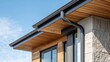 © Zarana  - Modern house exterior featuring black gutters, wooden soffits, and stone cladding against a blue sky