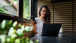 © Arianne - Woman working remotely using phone and laptop