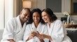 © GHM_STUDIO - Diverse friends in white bathrobes smiling at a smartphone while relaxing on a sofa in a spa or home setting.
