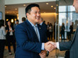 © Abzhat Zhussupov - smiling asian businessman in a blue suit shaking hands with a colleague in a modern office lobby during a networking corporate event, smiling with a blurred background of people