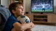 © Unimaginable Pic - Young boy sitting on living room floor hugging a soccer ball while watching a sports match on TV