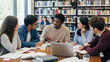 © Rafly - Diverse university students discussing group project together in modern library study space