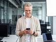 © Kin-Studio - Smiling young businessman in glasses using a mobile phone in a bright modern office setting.