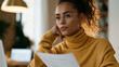 © forenna - Young professional reviews a federal loan adjustment letter at a modest apartment dining table, a budget spreadsheet visible on a nearby laptop screen, the quiet moment capturing