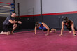 © wavebreak3 - Male coach instructing two female trainees doing push-ups in sportswear on red mat with orange band