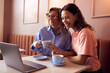 © Flamingo Images - Two multicultural smiling friends in a cozy cafe share a smile over coffee and a laptop, enjoying a casual moment together