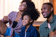 © Jovo Jovanovic/Stocksy - Family enjoys watching something together, all smiling.