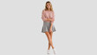 © Vyatcheslav - Young woman in a pink sweater and grey pleated skirt standing on a light background. Casual fashion portrait of a smiling blonde female model. Copy space