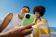 © BONNINSTUDIO/Stocksy - Happy friends sharing phone screen at beach vacation