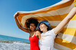 © BONNINSTUDIO/Stocksy - Happy friends enjoying summer day at beach holding towel