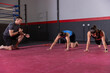 © wavebreak3 - Male trainer guiding two female trainees crawling on large red mat at gym near boxing ring