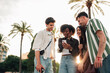 © Zamrznuti tonovi - Diverse young friends smiling and looking at a smartphone screen, sharing a moment and enjoying a digital connection outdoors