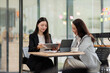 © David - Asian businesswomen collaborating on a digital tablet, discussing project ideas and strategy in a modern office meeting, demonstrating teamwork and digital innovation