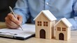 © Yi - Man signing real estate contract with wooden model houses on desk, home buying mortgage agreement concept