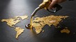 © mihrzn - Hand holding fuel nozzle pouring oil onto a glittering gold world map against dark background.