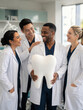 © SerPak - A cheerful dental team in white lab coats smiles while holding a large tooth model in a modern clinic. Teamwork and dental care.