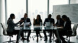 © REAL  - Soft focus blurred photo of Silhouettes of business people in a corporate meeting sitting around a table in a modern office with large bright windows